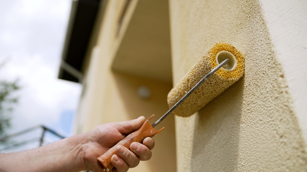 A man using a roller to paint a house’s exterior.
